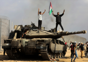 Photo datant du 7 octobre 2023. Des habitants de Gaza ont franchi les clôtures, et deux d'entre eux sont debout sur un char d'assaut, les bras en l'air. L'un des deux hommes brandit un drapeau palestinien.